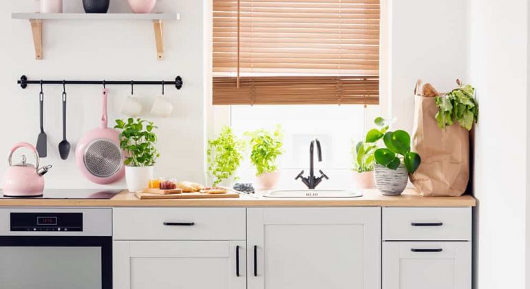 Real photo of a kitchen cupboards, countertop with plants, food, and shopping bag, and window with blinds in a kitchen interior
